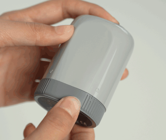 Hand holding Sibionics blood glucose monitor on arm. Grey device, easy to use.