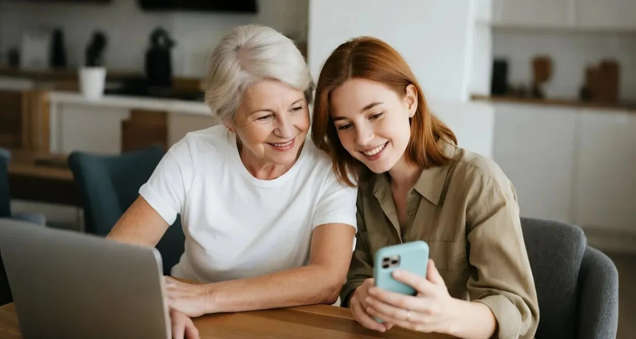 Two women in a kitchen, one using a laptop and the other a phone, suggesting a tech - savvy, family - friendly environment for Sibionics blood glucose monitors.